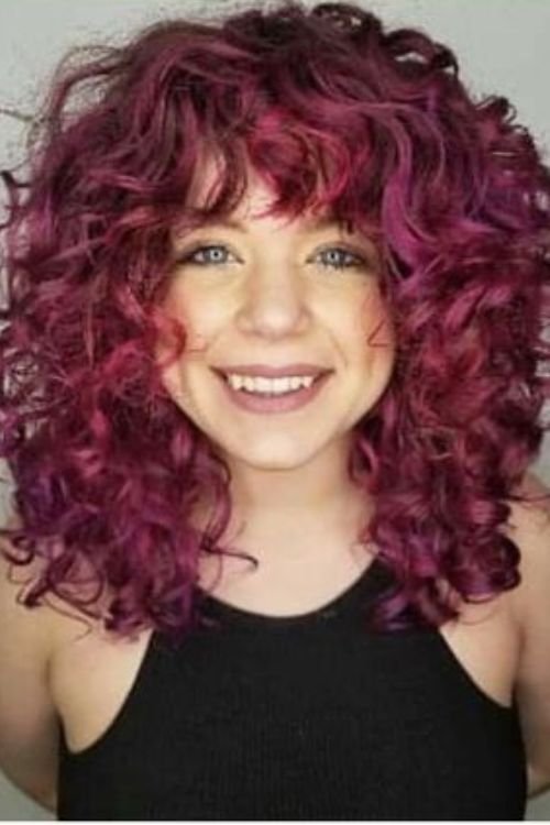 Curly wolf cut with vibrant magenta curls layered volume and tousled bangs