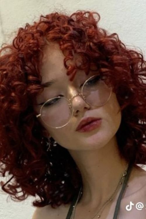 Curly wolf cut with vivid red curls and soft bangs